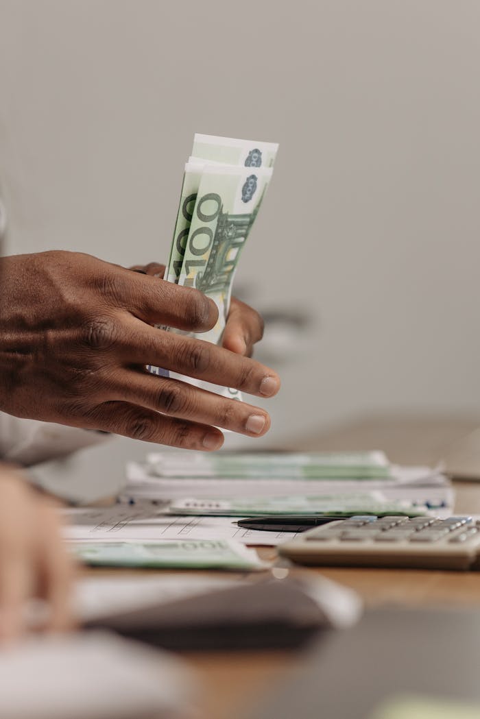 Close-up of hands counting US dollar bills on a cluttered desk in an office setting.